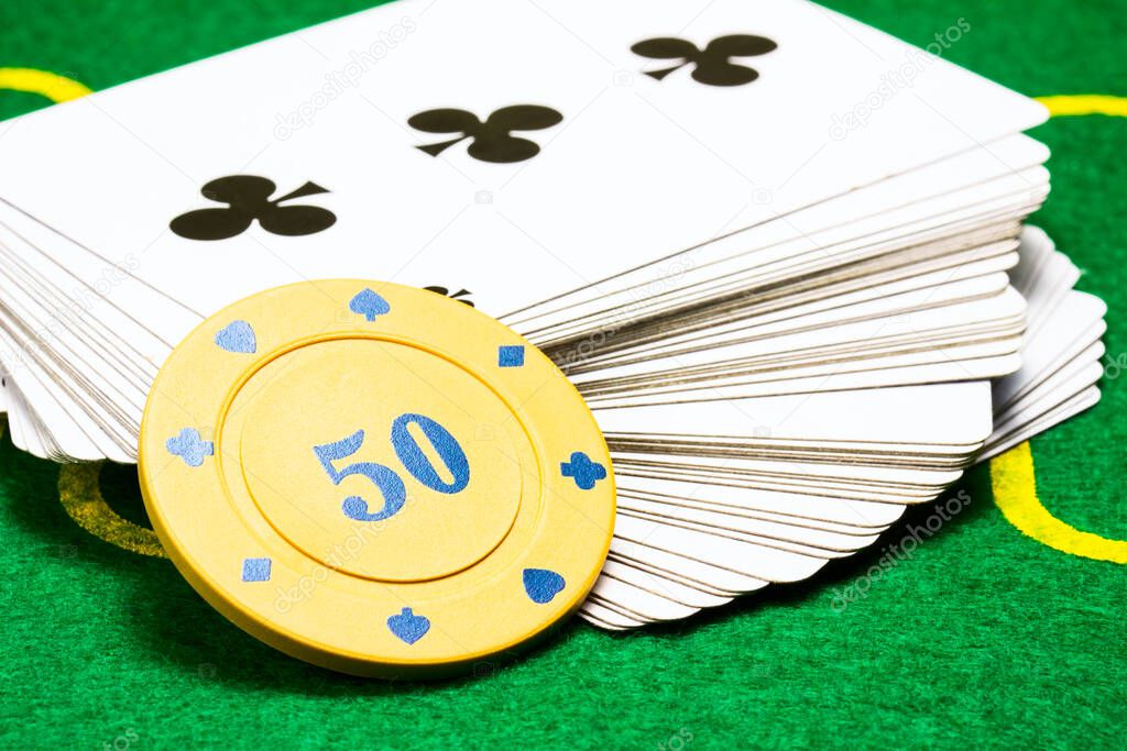 yellow poker chip on a deck of playing cards closeup on a bright green canvas concept of board games and casino