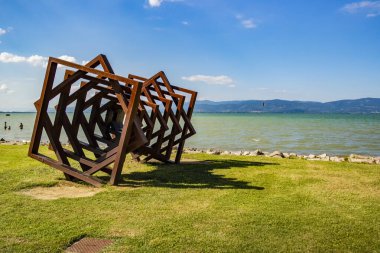 Sanatçı Michele Ciribifera 'nın Twister adlı metal eseriyle Trasimeno Gölü manzarası. 16 Haziran 2018 Castiglione del Lago, Umbria - İtalya
