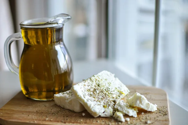Close up of feta cheese(Greek cheese) slices on a wooden serving board and a bottle of olive oil in nature light — Stock Photo, Image