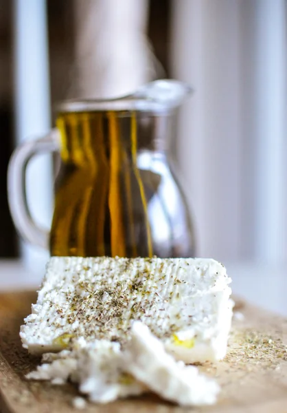 Close up de queijo feta (queijo grego) fatias em uma tábua de serviço de madeira e uma garrafa de azeite na luz da natureza — Fotografia de Stock