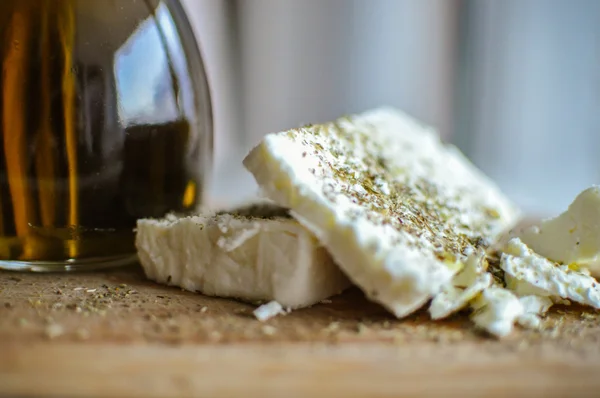 Primer plano de rebanadas de queso feta (queso griego) en una tabla de servir de madera y una botella de aceite de oliva en luz natural —  Fotos de Stock