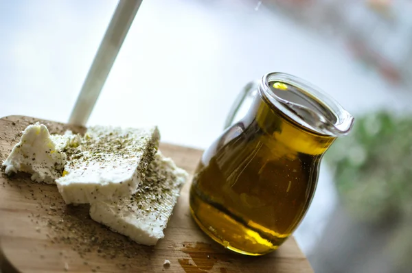 Close up of feta cheese(Greek cheese) slices on a wooden serving board and a bottle of olive oil in nature light — Stock Photo, Image