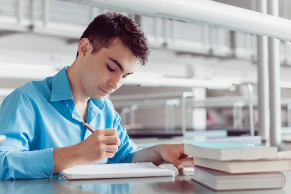 Ung man studenternas lärande tar anteckningar på bibliotek — Stockfoto