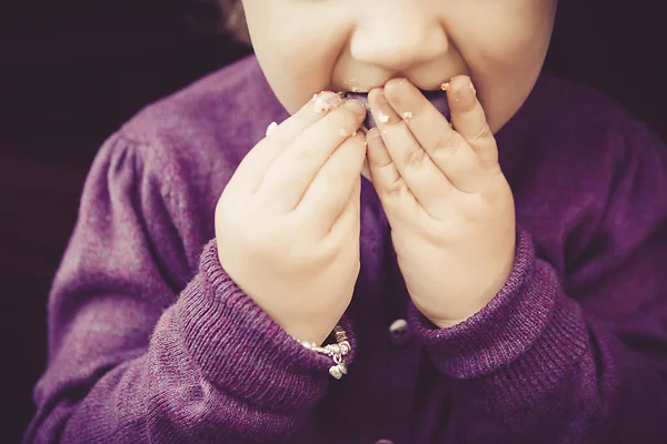 Linda niña comiendo macarrones dulces con el dedo sucio — Foto de Stock