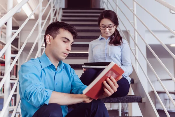 Eleverna läser bok tillsammans i biblioteket — Stockfoto