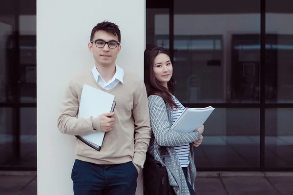 Deux étudiants attrayants parlent et regardent dans le dossier à l'extérieur du bâtiment du campus — Photo