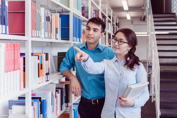 Universitaire studenten in de bibliotheek op zoek naar een boek — Stockfoto