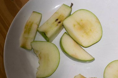 Elmalar beyaz bir tabakta, masada.