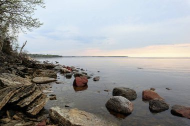 Sakin bir gölde, kayalık bir sahilde güzel bir gün batımı.