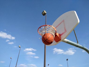 Bir basketbol topu ağla çemberden dışarı atılır. Arka planda elektrik direkleri ve gökyüzü.
