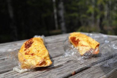 Ahşap bir masanın üzerinde iki tane ev yapımı paket. Orman arka planda