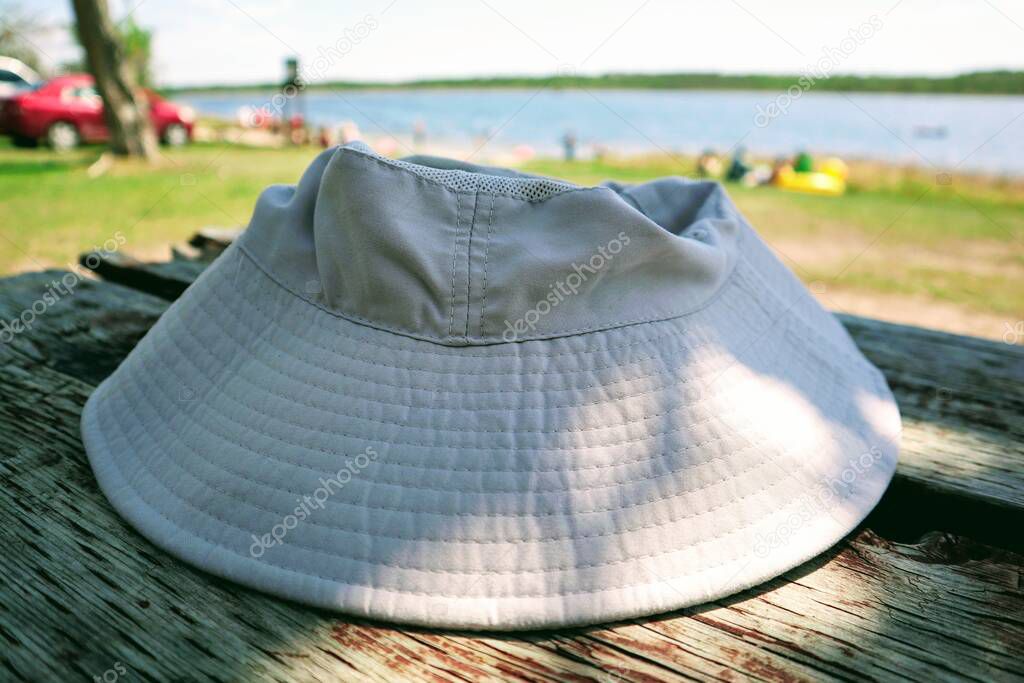 Close-up of a hat lies on a wooden table. Vacationers and a lake in the background.