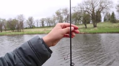 Çocuk elleri oltadaki bir oltayla misinayı çözer. Arka planda orman ve nehir.