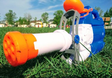 Su tabancasının yakın çekimi yeşil çimlerin üzerinde. Arka planda bank ve oyun alanı.