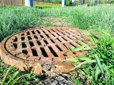 Paslı bir kanalizasyon kapağına yakın çekim. Arka planda yeşil çimen.