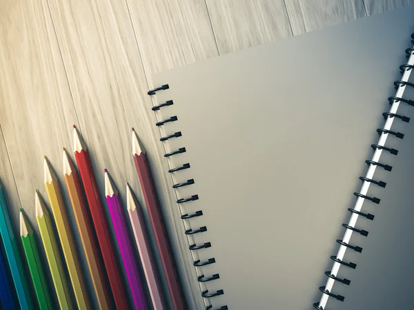 Lápis de cor no caderno verificado no fundo de madeira — Fotografia de Stock