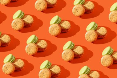 Turuncu arkaplanda sert ışıkta turuncu ve yeşil makaronlar var.