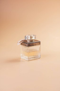 Pastel sarısı arka planda parfüm kutusu olan altın bir kozmetik şişesi.