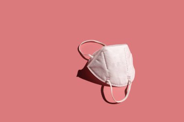 Bir FFP2 solunum koruma maskesi, pembe yüzeyde beyaz.