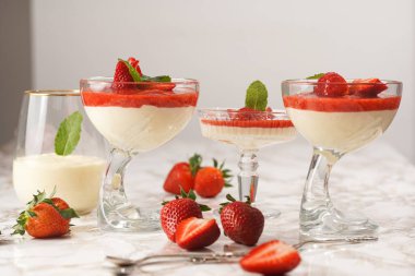 Geleneksel kremalı tatlı panna cotta ile birkaç bardak naneli ve çilekli reçelli mermer yüzeyde taze çilek