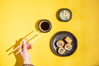 Soja soslu, zencefilli ve çubuklu kadın eli ile siyah tabakta somon ve tobiko ile suşi rulosu.