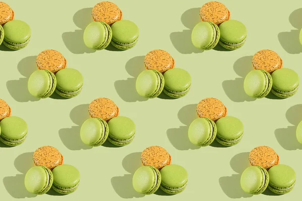 Hard light pattern of a macaroon pastry - two green ones and one orange - photographed on light green surface