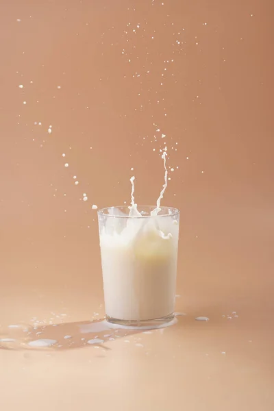 A glass of milk and splashes of milk on pastel yellow background