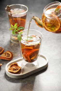 Siyah çay, portakal ve nane ile dolu şeffaf bir çaydanlık bir bardağa çay döküyor.