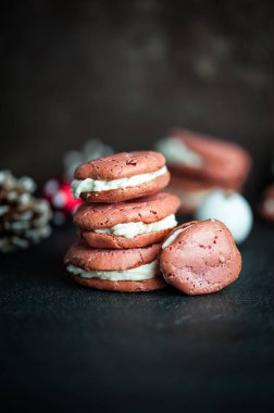 Koyu bir yüzeyde üst üste yığılmış beyaz kremalı birkaç pembe çatlamış kurabiye.