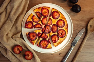 Dilimlenmiş yuvarlak bir pasta, beyaz bir tabakta erikler, tahta bir masa, üst bir manzara.