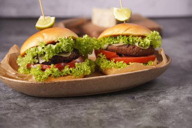 Vejetaryen köfteli iki hamburger, marul, domates ve tahtanın üzerinde bir dilim limon.