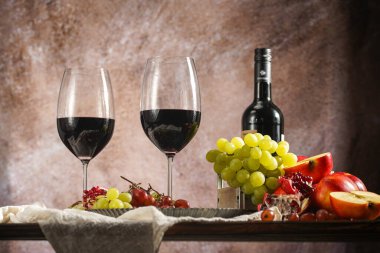 İki kadeh kırmızı şarap, bir şişe şarap ve meyve seçimi: elma, üzüm, nar. Durgun hayat