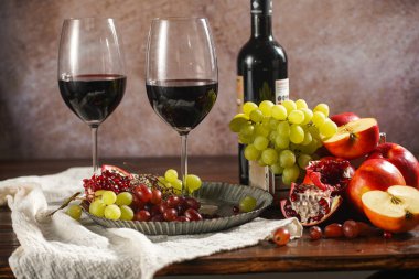 İki kadeh kırmızı şarap, bir şişe şarap ve meyve seçimi: elma, üzüm, nar. Durgun hayat