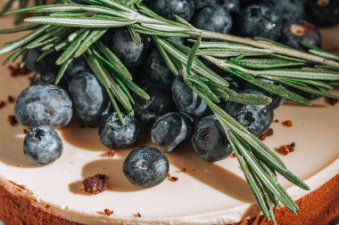 Yuvarlak karamelli kekin üst tarafında yaban mersini ve biberiye dalları var.