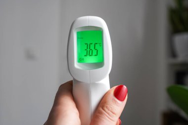 Alnın termometresini tutan bir kadın el vücut ısısı 36,5 derece, yeşil.
