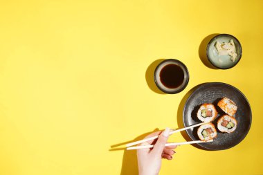 Suşi nigiri, siyah tabakta soya soslu, zencefilli ve yemek çubuklu kadın eli.