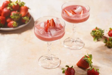 İki bardak kırmızı çilekli tatlı, buz küpleri, kırılmış buz ve çilek dilimleri.