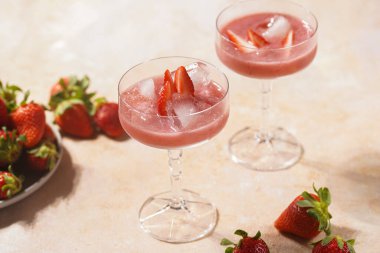 İki bardak kırmızı çilekli tatlı, buz küpleri, kırılmış buz ve çilek dilimleri.