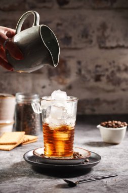 Kadın eli, buzlu ve kahveli bir bardağa süt döküyor.