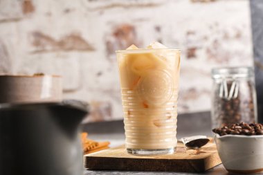 Tahtada buz küpleri ve sütlü kahve olan bir bardak.