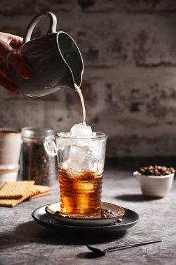 Kadın eli, buzlu ve kahveli bir bardağa süt döküyor.