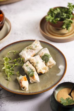 Yeşil tabakta pirinç kağıdında tavuk, havuç ve bambu filizi, susam sosu ve beton yüzeyde kişniş içeren birkaç yumurta rulosu.