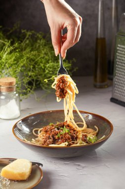 Yeşil kasede kekik ile süslenmiş bolonez soslu spagetti ile çatalı tutan bir el.