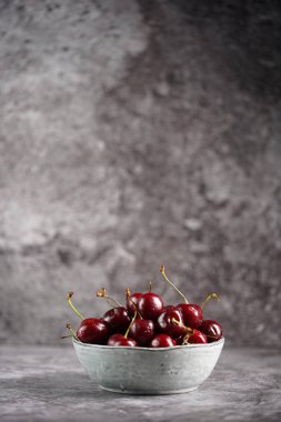 Gri arka planda gri bir tarama kabında taze ve ekşi koyu kırmızı kirazlar.