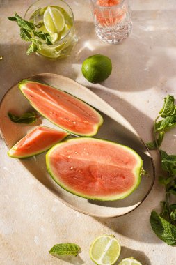 Sabah karanlığında karpuz dilimleri, kireç ve nane şekeri kum renkli yüzeyde.