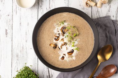 Kekikli mantar çorbası, ekşi krema ve kızarmış şampiyonlar beyaz ahşap bir masada koyu siyah bir kase içinde, üst manzara