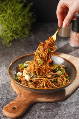 İtalyan spagettisi, tavuk, yeşil fasulye, peynirli mozzarella ve yeşil kase içinde gri beton yüzeyde tahta üzerinde taze kekik ile çatal tutan kadın eli.