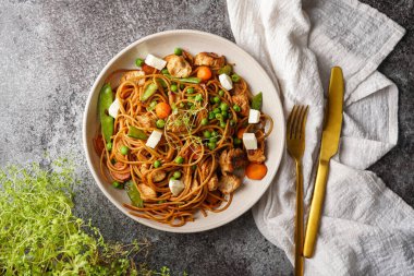 İtalyan makarna spagettisi tavuk, yeşil fasulye ve peynir mozzarella ve gri beton yüzeyde açık gri kase, altın çatal bıçak takımı ve bej renkli peçete, üst manzara.
