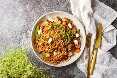 İtalyan makarna spagettisi tavuk, yeşil fasulye ve peynir mozzarella ve gri beton yüzeyde açık gri kase, altın çatal bıçak takımı ve bej renkli peçete, üst manzara.