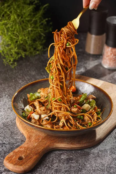 İtalyan spagettisi, tavuk, yeşil fasulye, peynirli mozzarella ve yeşil kase içinde gri beton yüzeyde tahta üzerinde taze kekik ile çatal tutan kadın eli.